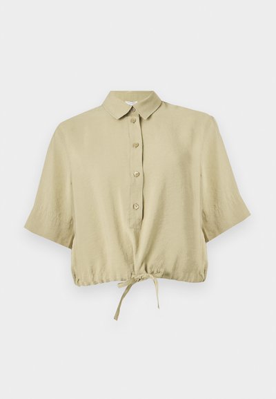 Chemisier court beige à manches courtes, avec col, patte de boutonnage et lien réglable à l'ourlet, présenté sur fond blanc.