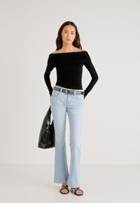 Zwarte off-shoulder top met lange mouwen, lichtblauwe flared jeans, zilverkleurige gespste riem, glanzende zwarte tas en zwarte platte sandalen.