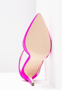 Chaussure à talon haut rose vif avec bout pointu, montrée semelle vers le haut sur un fond blanc en coin.