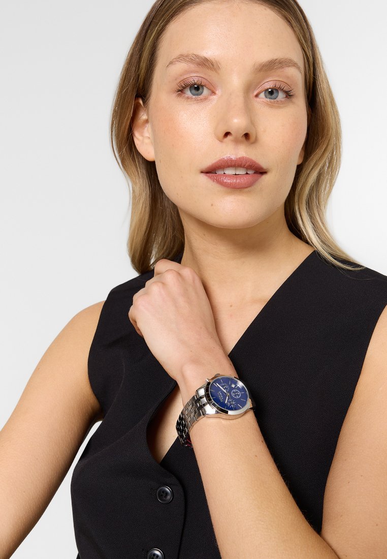 Reloj de pulsera metálico con un dial azul, pulsera de eslabones plateada y herrajes en tono plateado. Presenta manecillas de horas, minutos y segundos.