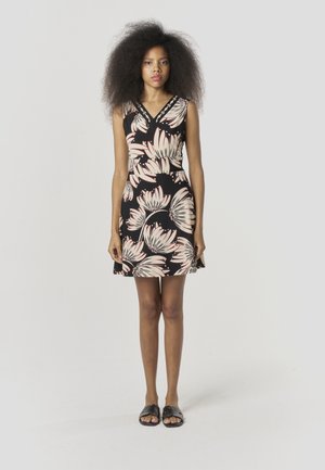 Virágos ruha fekete alapon, nagy rózsaszín és fehér virágokkal, V-nyakkivágással és testhezálló derékkal; fekete lapos szandállal párosítva.