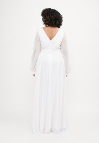 Langes weißes Kleid mit einem taillierten Oberteil und tiefem V-Ausschnitt am Rücken, durchsichtigen, luftigen Ärmeln und einem fließenden Rock mit gerafftem Taillendetail.