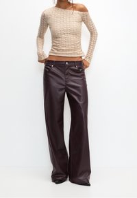 Top in pizzo beige a maniche lunghe con design off-shoulder, abbinato a pantaloni in pelle bordeaux scuro a gamba larga con tasche frontali e dettagli in argento.