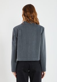 Grå kort jakke med en strukturert design, lange ermer og et subtilt teksturert stoff, kombinert med svarte høyt midje bukser.