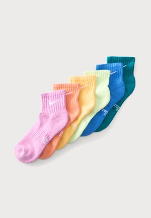 Seks par ribstrikkede crew-strømper i pastelfarver arrangeret på en række fra pink til teal, hver med et lille hvidt Nike-logo.
