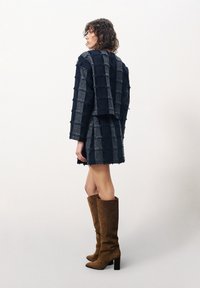 Marineblauw en grijs geblokt stoffen outfit met rafelige randen; model draagt bruin suède kniehoge laarzen met een chunky hak.