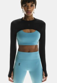 Sort langærmet top lagdelt over en lysblå crop top med skåret design. Matchende lysblå højtaljede leggings med logo-detalje.