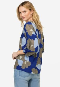 Camicia a stampa floreale nei colori blu, grigio e beige, con una vestibilità ampia, maniche a tre quarti e scollatura rotonda.