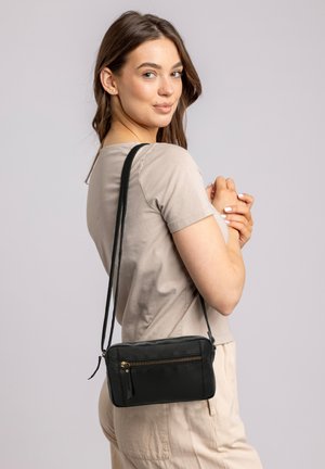 Black leather crossbody bag with a zippered front pocket, rectangular shape, smooth texture, and adjustable strap, worn at the shoulder.