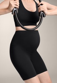 Črni komplet aktivne športne obleke za nosečnice vključuje oprijet top in hlače z visokim pasom. Material je gladek in raztegljiv ter nudi oporo med vadbo.