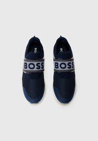 Ténis de desporto azul-marinho com parte superior em malha, faixa elástica com o logótipo "BOSS", silhueta arredondada e sola branca. Design robusto e moderno.
