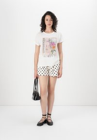 White graphic T-shirt featuring floral design and text, paired with polka dot shorts, black flats, and a small black bag.