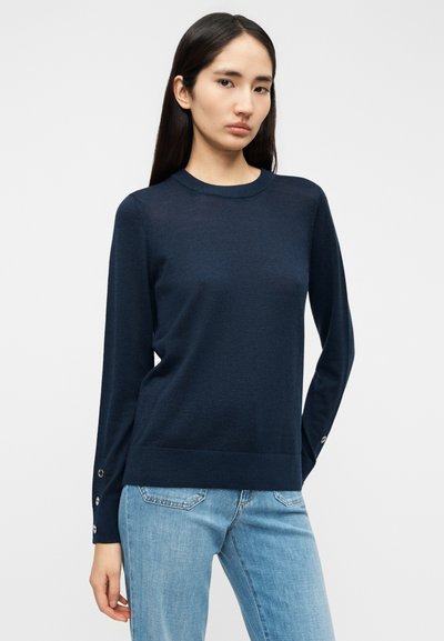 Μπλε πουλόβερ σε σκούρο μπλε χρώμα, πλεκτό, με στρογγυλή λαιμόκοψη, μακριά μανίκια και λεπτομέρειες με κουμπιά στις μανσέτες. Μαλακή υφή και εφαρμοστή γραμμή.