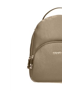 Zaino in pelle color khaki con forma arrotondata, dotato di due scomparti con zip e manico superiore. Design minimalista con logo in rilievo.