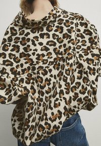 Leopardprint-top i beige med sorte og brune pletter. Har en løs pasform og en draperet halsudskæring. Stoffet ser glat og let ud.