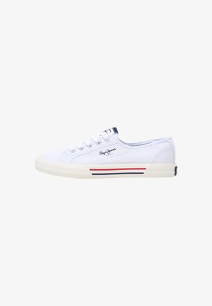 Vita kanvas sneakers med låg profil, utrustade med gummisula, snörning och röda samt marinblå ränder längs basen. Varumärkeslogotyp närvarande.