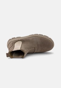 Botă din suede maro până la gleznă, cu panouri elastice laterale, un interior texturat și o talpă din cauciuc rezistentă. Vârf rotund cu un bucluc pentru a fi ușor de purtat.
