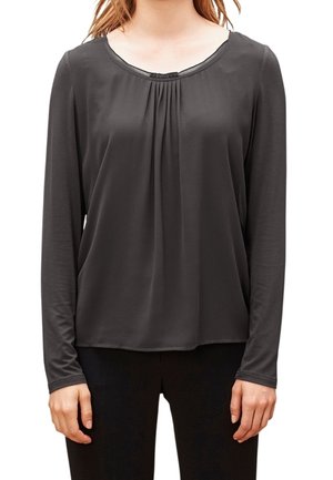 Donkergrijze blouse met lange mouwen en een ronde hals, zachte textuur, geplooid detail in het midden en een losse pasvorm, gecombineerd met een donkere broek.