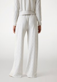 Witte sweatpants met een reliëfpatroon, wijde pijpen en zijkanten met strepen. Gemaakt van zachte stof; geribbelde tailleband en manchetten.