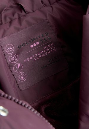Etikett innerhalb einer dunkelvioletten Jacke, das die Marke "UNLIMITED TEC", Pflegehinweise und den Text "HIGH PERFORMANCE GARMENTS" zeigt.