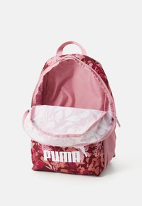 PUMA seljakott roosades toonides lillemustriga, kangast välimus, võrgusilm kotis külje tasku ja valge logo ees. Avatud ülaosa paljastab sisemuse voodri.