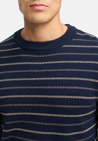 Mørkeblå strikket sweater med horisontale cremefarvede striber, rund halsudskæring, struktureret stof samt ribbede manchetter og kant.
