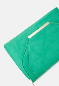 Clutch de ante verde con un acento metálico dorado, que presenta un diseño plegado y detalles de costura. Textura suave con una forma estilizada.