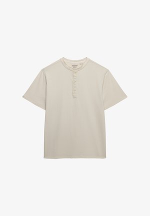 Chemise henley beige à manches courtes avec trois boutons et logo brodé discret sur la poitrine, sur fond blanc.