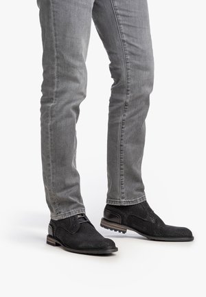 Zapatos de cuero negro texturizado con un acento liso, combinados con jeans gris ajustados. Los zapatos tienen una punta redondeada y una suela de perfil bajo.