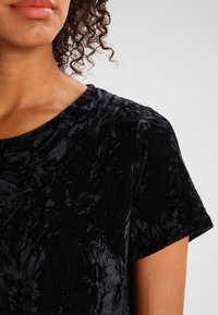 Top in velluto nero con una finitura morbida e testurizzata; maniche corte e scollatura rotonda. Una leggera lucentezza mette in risalto il design.
