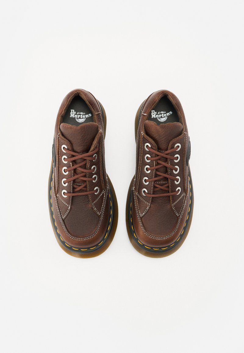 Braune Lederschuhe mit strukturiertem Finish, runder Zehenform und kontrastierenden gelben Nähten auf einer dicken schwarzen Sohle. Schnürsenkel und Logo sichtbar.