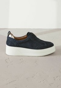 Marinblå mocka slip-on sko med en vit plattformssula, med en texturerad ovandel och en metallisk detalj vid klacken.