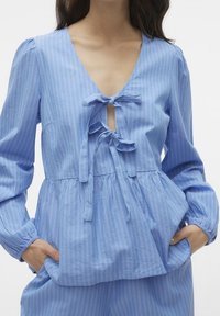 Light blue striped blouse with a deep V-neck, tie closure at the front, and long sleeves, featuring a gathered waist and soft texture.