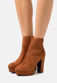 Bottines en suède marron avec un bout arrondi, une haute plateforme et un gros talon noir. Texture lisse et design simple sans embellissements.