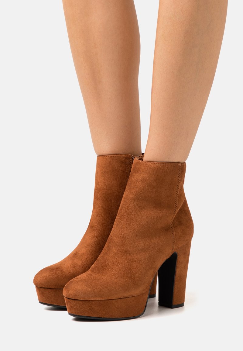 Bottines en suède marron avec un bout arrondi, une haute plateforme et un gros talon noir. Texture lisse et design simple sans embellissements.
