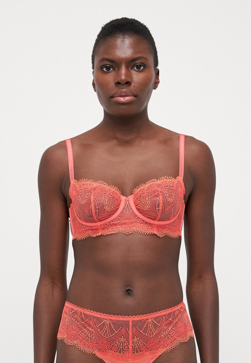 Soutien-gorge en dentelle corail avec armatures et bretelles réglables, présentant une broderie florale complexe et des bords en forme de vagues. Culotte en dentelle assortie incluse.