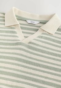 Suéter ligero de punto con escote en V y cuello corto. Presenta rayas horizontales alternadas en verde pálido y crema. Tejido texturizado.