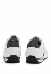 Zapatillas de cuero blancas con detalles en azul marino, con un perfil bajo, punta redondeada, suela de goma texturizada y logotipo en el talón.