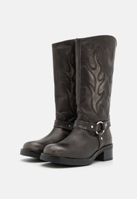 Botoși din piele maro, până la genunchi, cu broderie în formă de flacără, bretele la gleznă cu închidere metalică, toc mic și textură netedă.