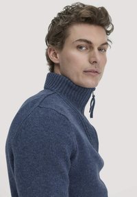 Dunkelblauer Strickpullover für Herren mit hohem Kragen, ausgestattet mit einem Reißverschluss und Rippstruktur, Schulternähten und einer taillierten Silhouette.
