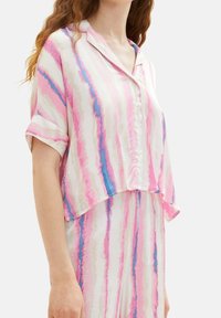 Camicia a maniche corte rosa e bianca con strisce astratte blu e rosa. Tessuto leggero e vestibilità rilassata. Collare rotondo e chiusura frontale con bottoni.