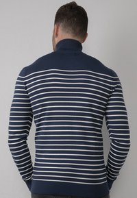 Maglione a strisce blu navy e bianche con colletto alto, maniche lunghe e polsini e orlo a costine, realizzato in un materiale morbido e lavorato a maglia.