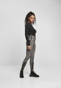 Top nero a maniche lunghe abbinato a leggings neri e grigi con effetto tie-dye a vita alta. Modella che indossa scarpe da ginnastica nere. Sfondo semplice.