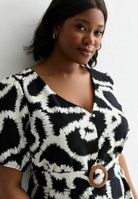 Robe à motifs noir et blanc avec un col en V, des manches courtes et une ceinture tissée avec une boucle ronde. Tissu doux avec un design texturé.