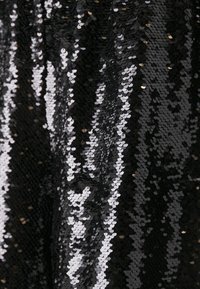 Tissu noir pailleté présentant un mélange de sequins circulaires noirs brillants et argentés, réfléchissant la lumière dans un motif texturé et superposé.