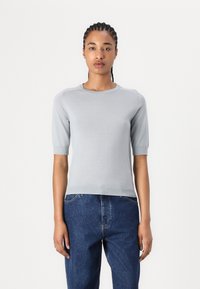 Pulover tricotat gri deschis cu mâneci scurte, guler rotund și tiv cu textură canelată. Asortat cu blugi denim blue. Textură netedă, design casual.