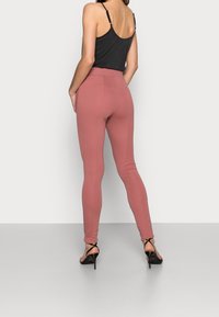 Rosa leggings med en mjuk yta, hög midja och smal passform. Bärs med en svart linne och svarta sandaler med remmar.