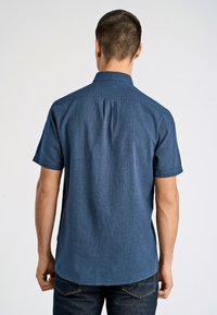 Koszula z krótkim rękawem, z kołnierzykiem w ciemnoniebieskim denimu, z subtelną teksturą. Posiada plisę na plecach i dopasowane przeszycia.