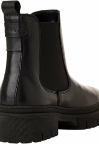 Botín Chelsea de piel negra con paneles laterales elásticos, suela de goma gruesa y tira de tracción. Textura suave y silueta estilizada.