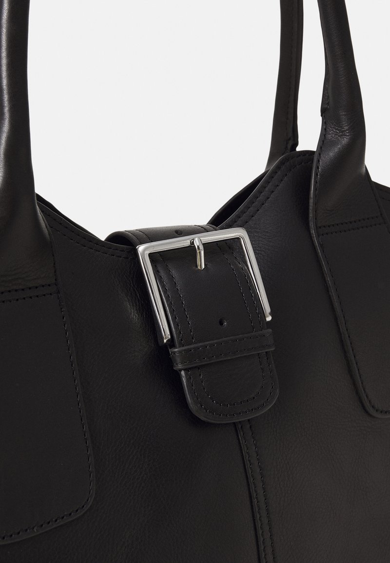 Sac à main en cuir noir avec deux poignées et une boucle rectangulaire argentée proéminente sur la sangle de fermeture à l’avant.